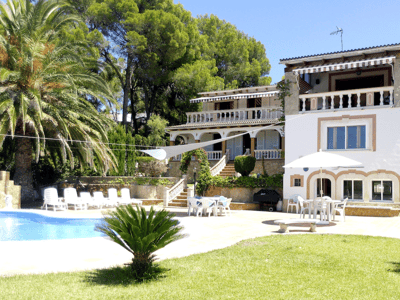 Vit medelhavsvilla med blå pool, solstolar och lummig grönska i bakgrunden.