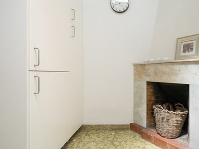 Rincón interior con chimenea de mármol, cesta de mimbre con leña y armario blanco alto.