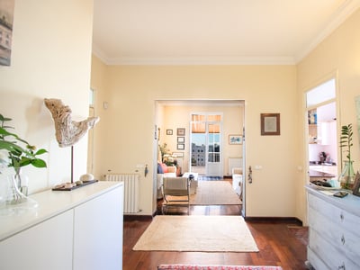 Pasillo con suelos de madera hacia una sala de estar soleada con sofás y acceso a un balcón exterior.