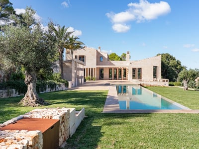 Villa moderne en pierre avec une longue piscine rectangulaire, pelouse verte et oliviers centenaires sous un ciel bleu.