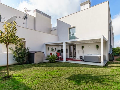 En modern vit byggnad med en grön gräsmatta och en täckt terrassyta med bubbelpool och matgrupp.