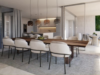 Large wooden dining table with cream chairs and glass pendant lights next to an open terrace and modern kitchen.
