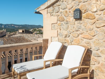Dos tumbonas blancas en una terraza de piedra con vistas a un pueblo mediterráneo y montañas.