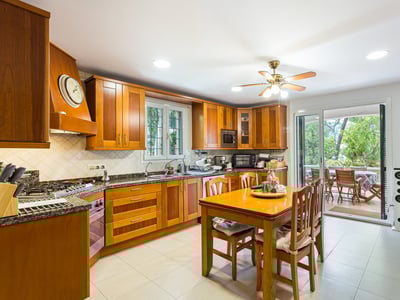 Traditionelle Holzküche mit Granitarbeitsplatten, Esstisch und Glastüren, die zu einer Terrasse führen.