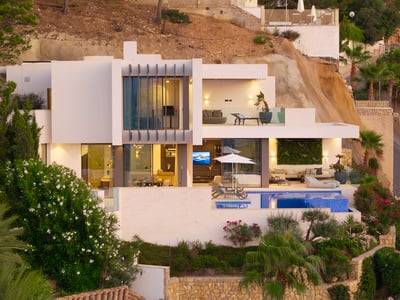 Modern white multi-level villa with a swimming pool, terraces, and large glass windows built into a rocky hillside.