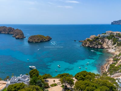Vista de una lujosa piscina infinita con borde de piedra, tumbonas modernas y vegetación exuberante. Arquitectura minimalista, cielo azul.
