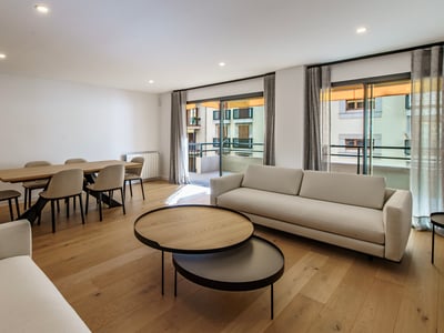 Modernt vardagsrum med vita soffor, soffbord i trä, matgrupp och stora fönster som leder till en balkong.