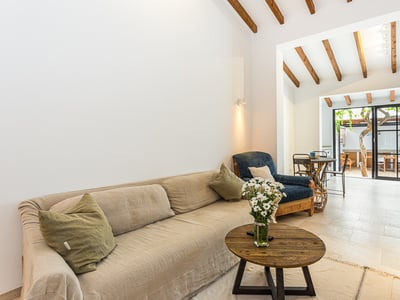 Living room with a beige sofa, wooden coffee table, exposed ceiling beams, and glass doors opening to a patio.