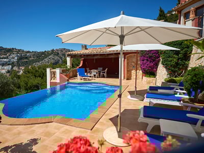 Terraza con piscina privada, hamacas azules y sombrillas blancas frente a un paisaje de colinas y cielo despejado.