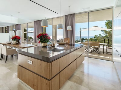 Modern kitchen featuring a wooden island, marble floors, and floor-to-ceiling glass walls overlooking the sea.