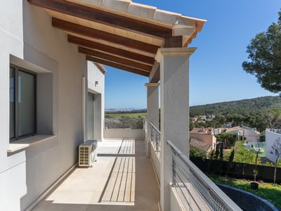 Lång övertäckt balkong med träbjälkar, vita väggar och metallräcke med utsikt över en grönskande dal.