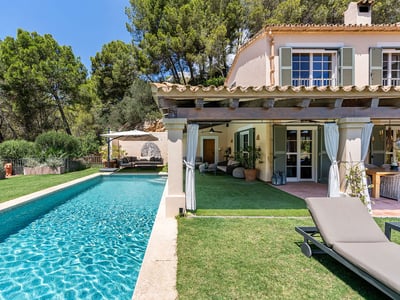 Rektangulär turkos pool bredvid en medelhavsvilla med täckt terrass och gröna fönsterluckor.