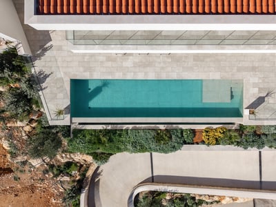 Bird's eye view of a turquoise swimming pool, stone terrace, terracotta roof, and lush Mediterranean landscaping.