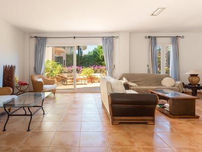 Amplio salón con sofás de mimbre, suelo de terracota y grandes ventanales que dan a una terraza soleada.