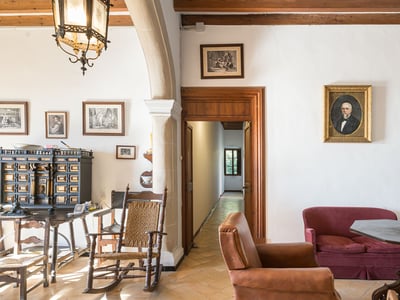Salón clásico con muebles antiguos, suelos de terracota, sofá de terciopelo rojo y retratos en las paredes.