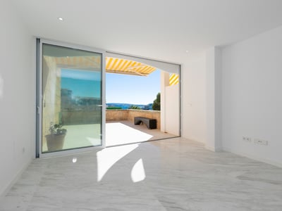 Heller leerer Raum mit weißen Marmorböden und einer großen Glasschiebetür, die auf eine sonnige Steinterrasse führt.