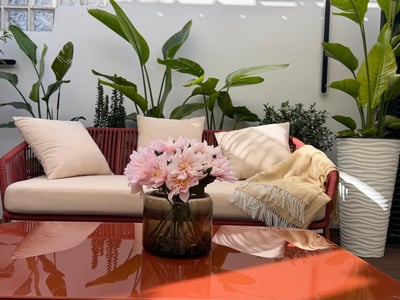 Red rope sofa with cream cushions on a terrace surrounded by tropical plants and a glossy orange coffee table.