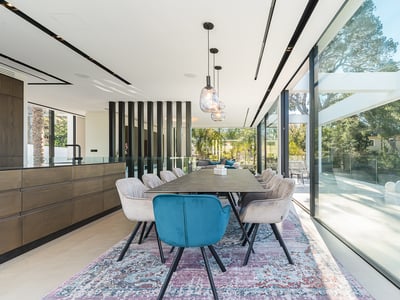 Heller Essbereich mit Designtisch, Samtsesseln in Blau und Beige und bodentiefen Glasfronten.