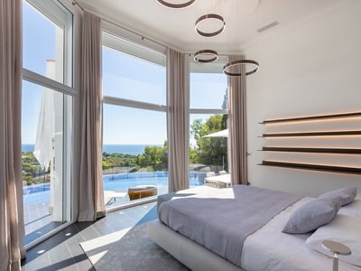 Modern master bedroom with floor-to-ceiling windows overlooking an infinity pool and the Mediterranean sea.