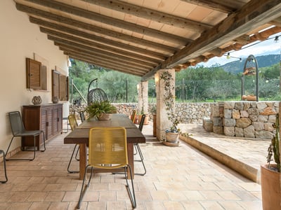 Covered terrace with wooden table, chairs, stone walls, and beamed ceiling overlooking the countryside.