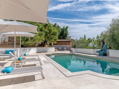 Moderner türkisfarbener Pool mit grauen Sonnenliegen, weißen Sonnenschirmen und einer großen blauen Buddha-Statue.