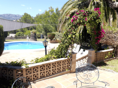 Oval pool omgiven av terrakottaplattor, en bougainvilleabåge och utsikt över bergen i bakgrunden.