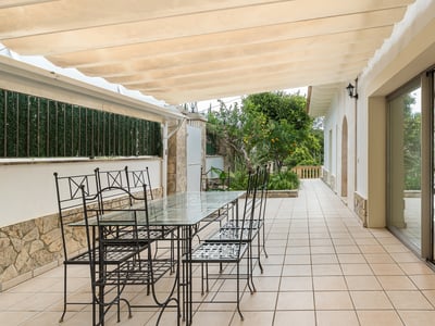 Terraza sombreada con mesa de comedor de cristal, sillas de metal negro y un toldo retráctil color crema.