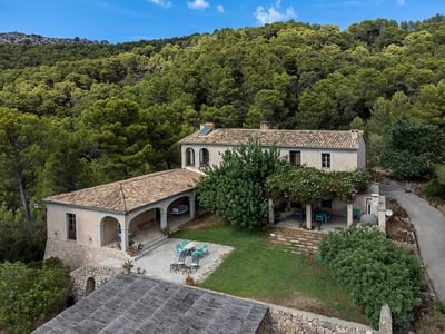 Elevated view of a Mediterranean stone villa with terracotta roof surrounded by a dense pine forest.
