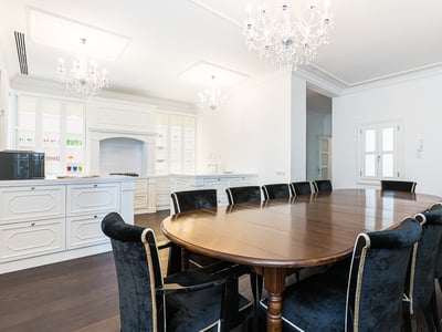 Großer ovaler Holztisch mit schwarzen Samtstühlen unter Kristallkronleuchtern in einem weißen Raum.