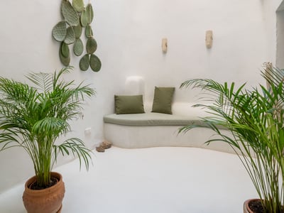 Banquette courbée en maçonnerie blanche avec coussins verts dans un patio minimaliste entouré de palmiers en pots.