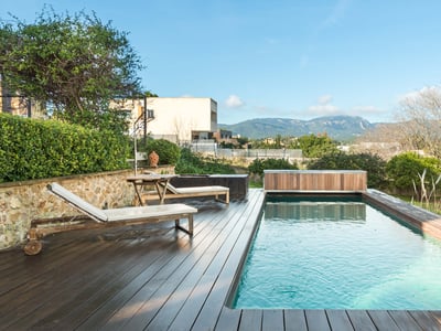 Piscina rectangular con terraza de madera oscura, tumbonas blancas y vistas panorámicas a la montaña.