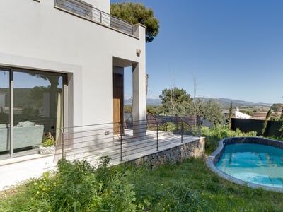 Modern vit villa med en kurvad blå mosaikpool, stenvägg och bergsutsikt under en klarblå himmel.