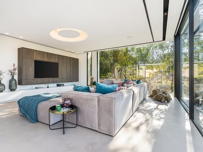 Modernes Wohnzimmer mit großem Sofa, TV-Wand und bodentiefen Fenstern mit Blick auf einen Garten.