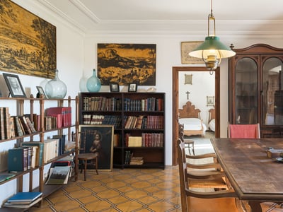Habitación clásica con gran mesa de madera, estanterías repletas de libros y suelo de baldosas decoradas.