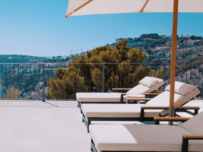 Luxury terrace featuring white sun loungers and a parasol next to an infinity pool overlooking the sea and cliffs.