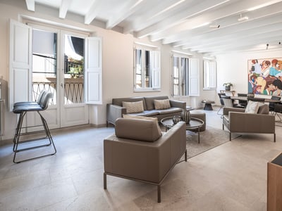 Salón luminoso con sofás de cuero gris, techo de vigas blancas y zona de comedor con una obra de arte colorida.