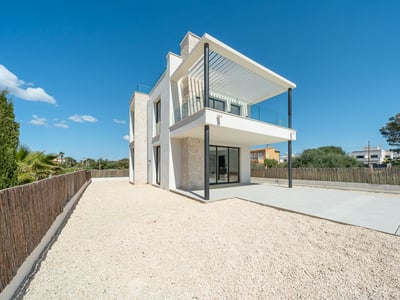 Two-story white modern villa with natural stone walls, a large balcony, and a gravel courtyard under a clear blue sky.