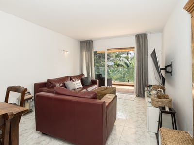 Modern living room featuring burgundy leather sofas, white marble floors, and a glass door view to a lush green balcony.