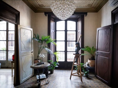 Großer Eingangsbereich mit hohen Holztüren, Mosaikböden, einem Kristallkronleuchter und Zimmerpflanzen.