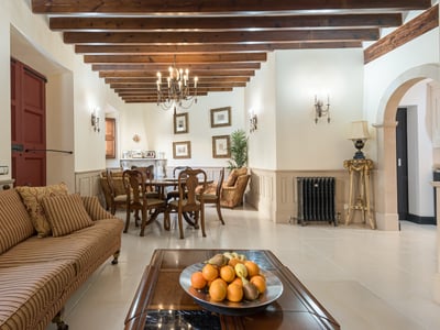 Amplio salón con vigas de madera vista, sofá de rayas y mesa de comedor bajo una lámpara de araña.