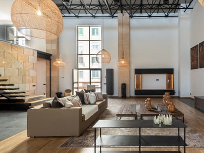 Modernes Wohnzimmer mit doppelter Deckenhöhe, beigen Sofas, Metallkamin und großen Rattan-Pendelleuchten.