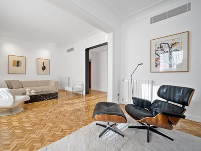 Bright living room featuring a cream sofa, black Eames chair, black marble table, and herringbone wood floors.
