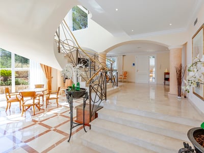 Helle Luxus-Eingangshalle mit weißer Marmortreppe, kunstvollen Eisenreben und Bogenarchitektur.