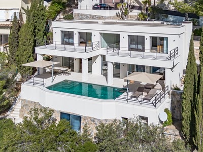 Elevated view of a white multi-level modern villa with a turquoise swimming pool on a stone terrace.