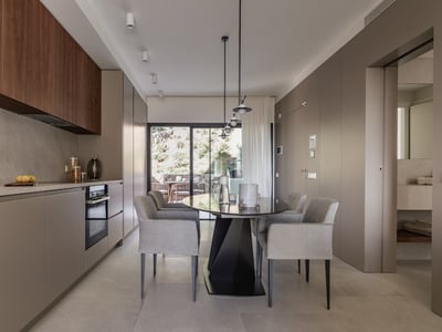 Minimalistische Küche mit taupefarbenen und Holzschränken, grauem Esstisch und großen Glastüren zur Terrasse.