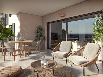 Terraza cubierta con sillones de mimbre, mesa de comedor de madera y grandes ventanales con vistas al mar.
