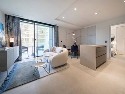 Sala de estar moderna con sofá curvo blanco, isla de cocina de piedra y grandes puertas de cristal hacia una terraza.