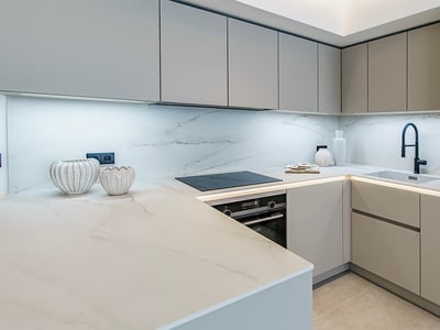 Una cocina moderna con armarios gris claro, encimeras de mármol blanco, iluminación LED y un grifo negro mate.