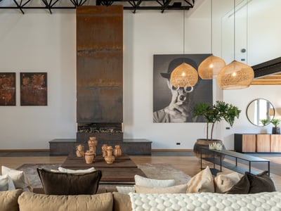 Geräumiges Wohnzimmer mit hohem Kamin aus verwittertem Stahl, beige Sofa und geflochtenen Pendelleuchten in einem Loft.