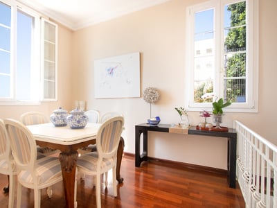 Comedor luminoso con mesa blanca, sillas a rayas, suelos de madera y grandes ventanales.